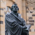 a statue of a man holding a book in front of a building