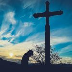 a person kneeling down in front of a cross