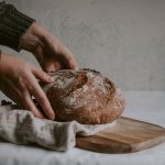 person holding brown bread on brown wooden chopping board