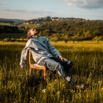 man in gray hoodie sitting on brown wooden chair on green grass field during daytime