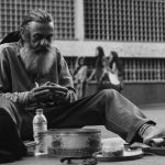grayscale photo of man sitting on ground with bottle