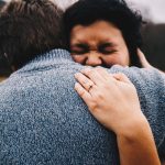 woman in gray knit sweater covering her face with her hand