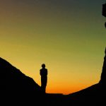 silhouette of man standing on rock formation during sunset
