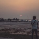 man wearing white t-shirt and blue jeans standing near field during sunset