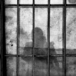 a shadow of a person behind bars in a jail cell