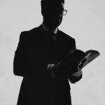a black and white photo of a man in a suit reading a book